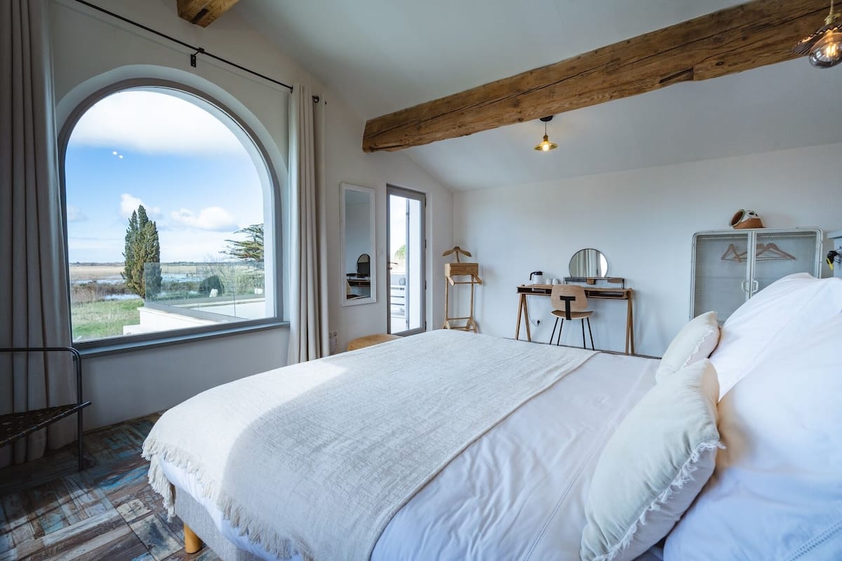 Une chambre avec une grande fenêtre, un lit, un bureau et une armoire.
