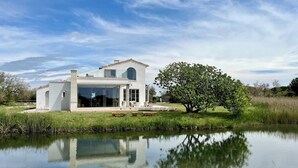 A modern house with a large glass window, a patio, and a pond in front. - Mas du Couvin - maison d'hôtes Camargue (Saintes-Maries-de-la-Mer)