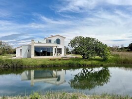 Una casa moderna con un amplio ventanal, un patio y un estanque al frente.