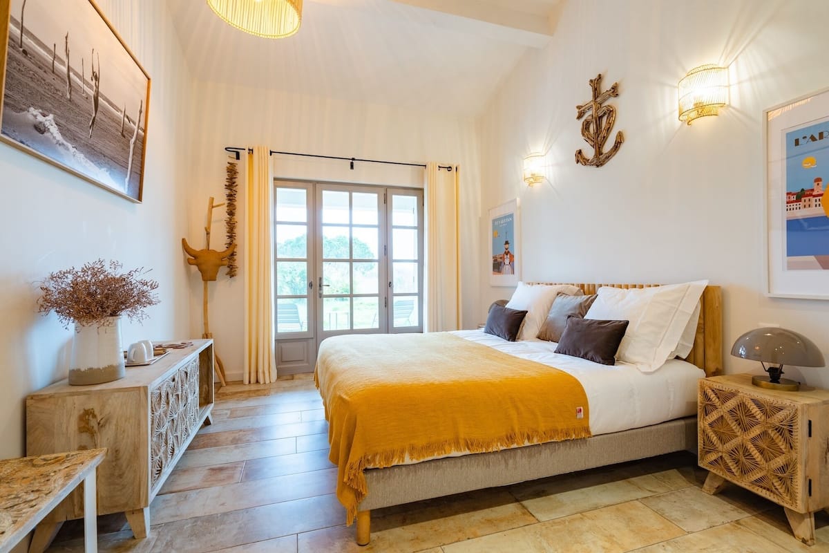 Une chambre à coucher avec un lit, une table de chevet, une lampe, des éléments décoratifs sur le mur et une vue à travers la porte.