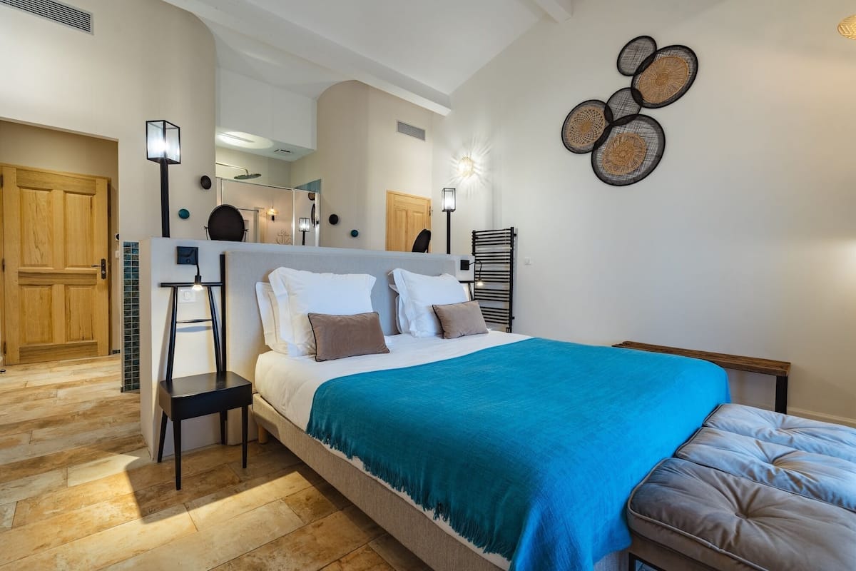 Une chambre à coucher comprenant un lit, des tables de chevet, un banc et un luminaire fixé au mur.