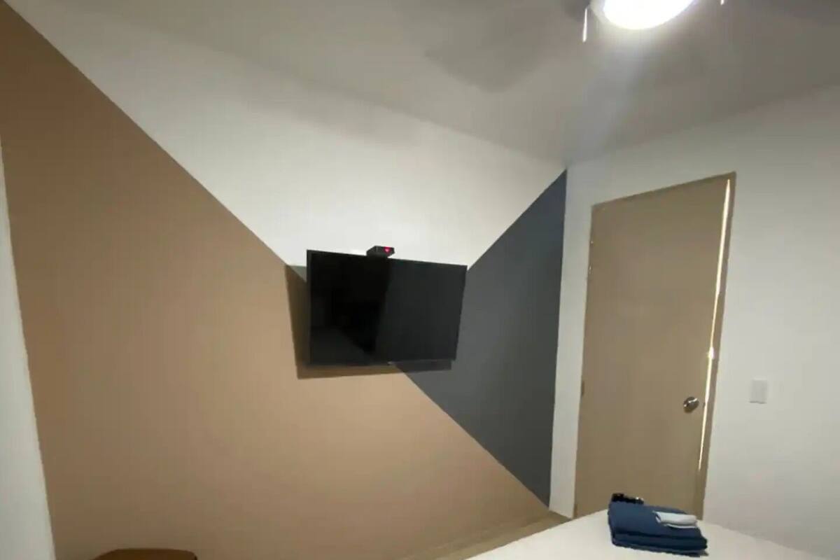 Ein Schlafzimmer mit Bett, Wandfernseher, einer Tür und einem kleinen Tisch.
