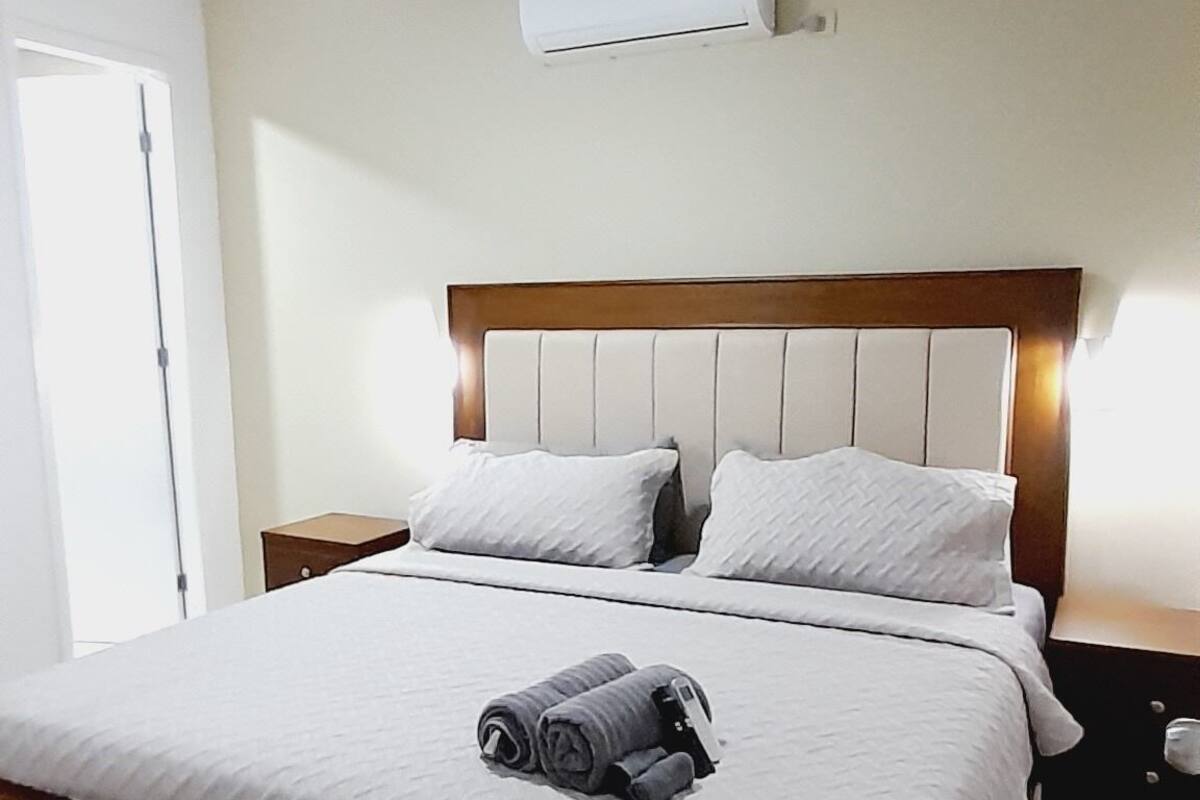 Ein Hotelzimmer mit einem großen Bett, einem Nachttisch, einer Klimaanlage und einer Tür.