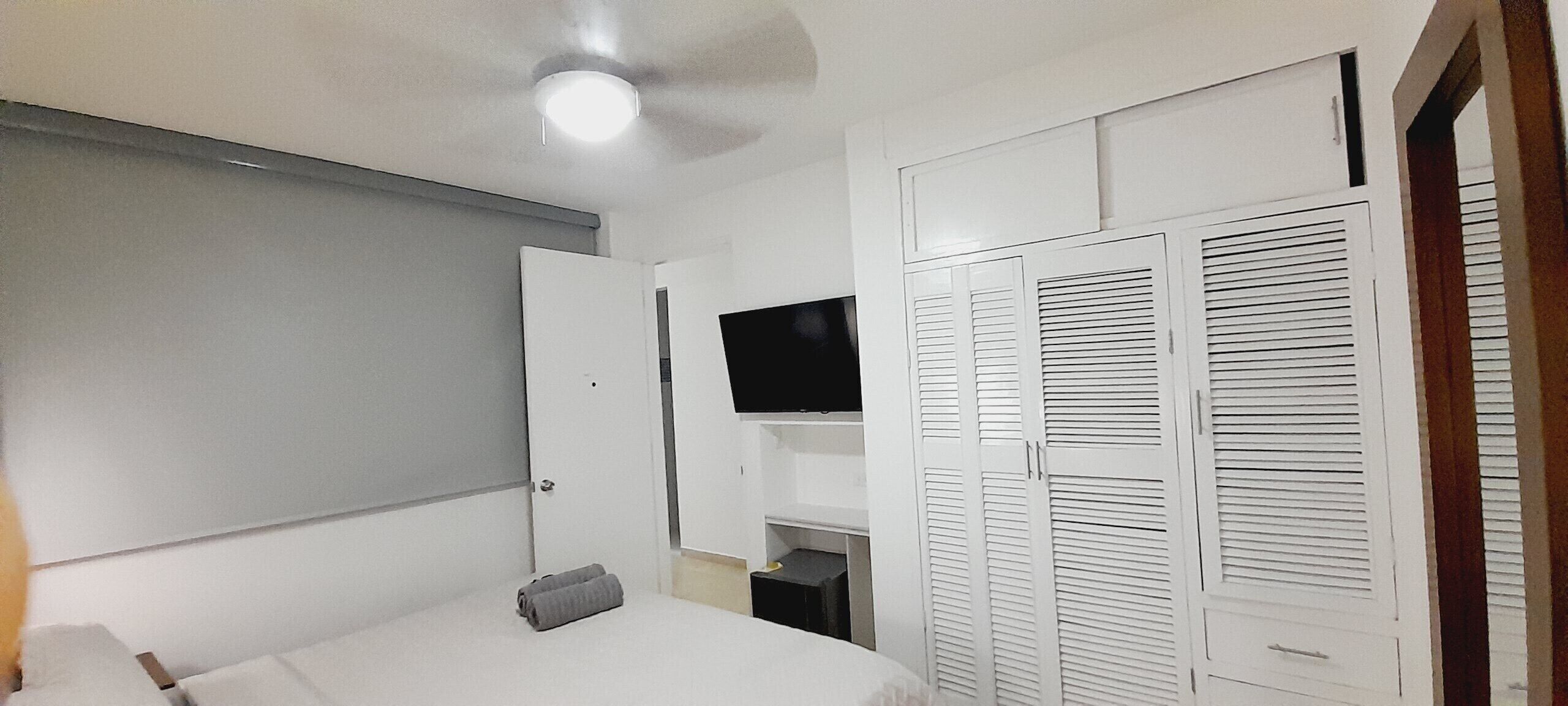 A bedroom with a bed, a wardrobe, a television, and a ceiling fan.