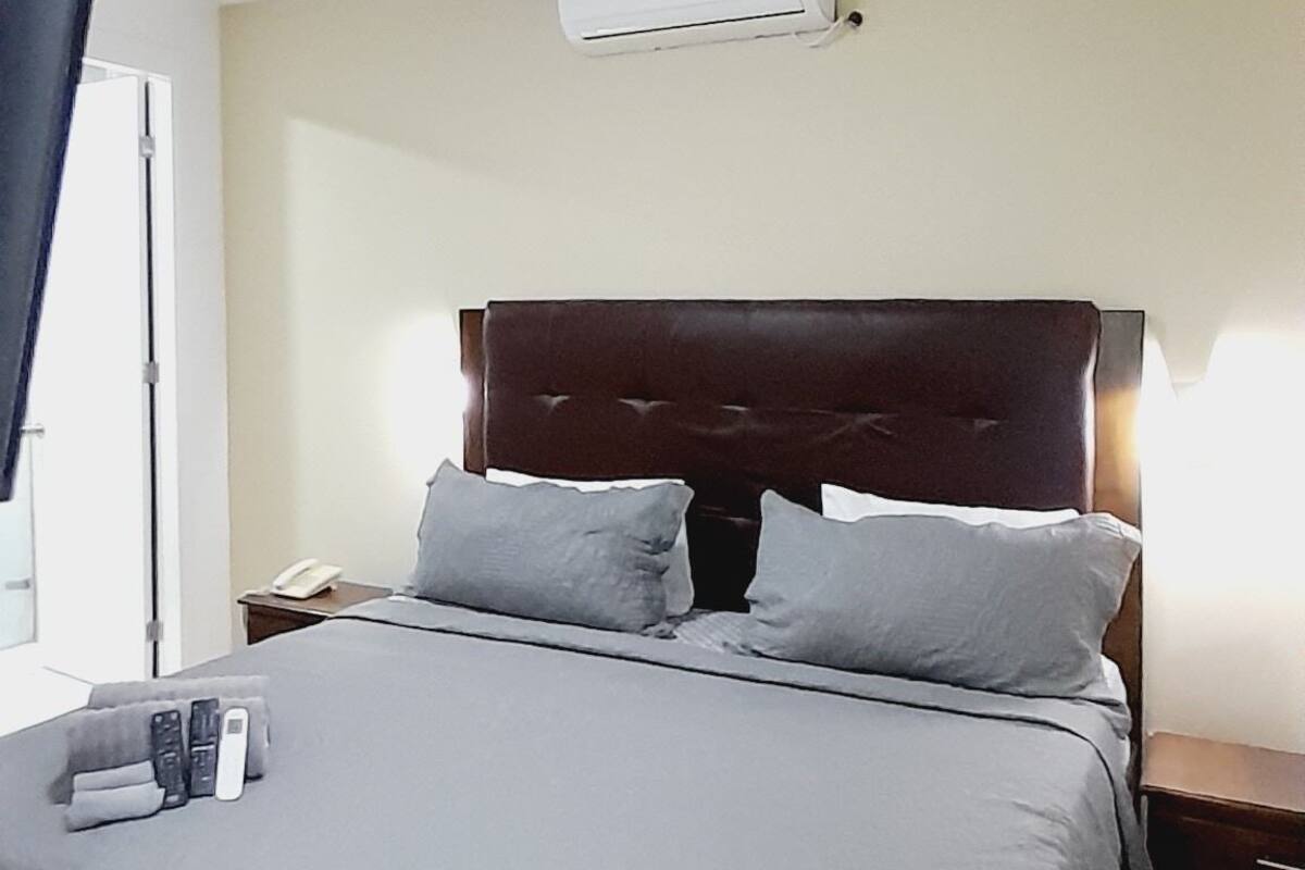Ein Hotelzimmer mit einem großen Bett, einem Deckenventilator, einer Klimaanlage, einem Nachttisch mit Lampe und einem Fenster mit Vorhängen.