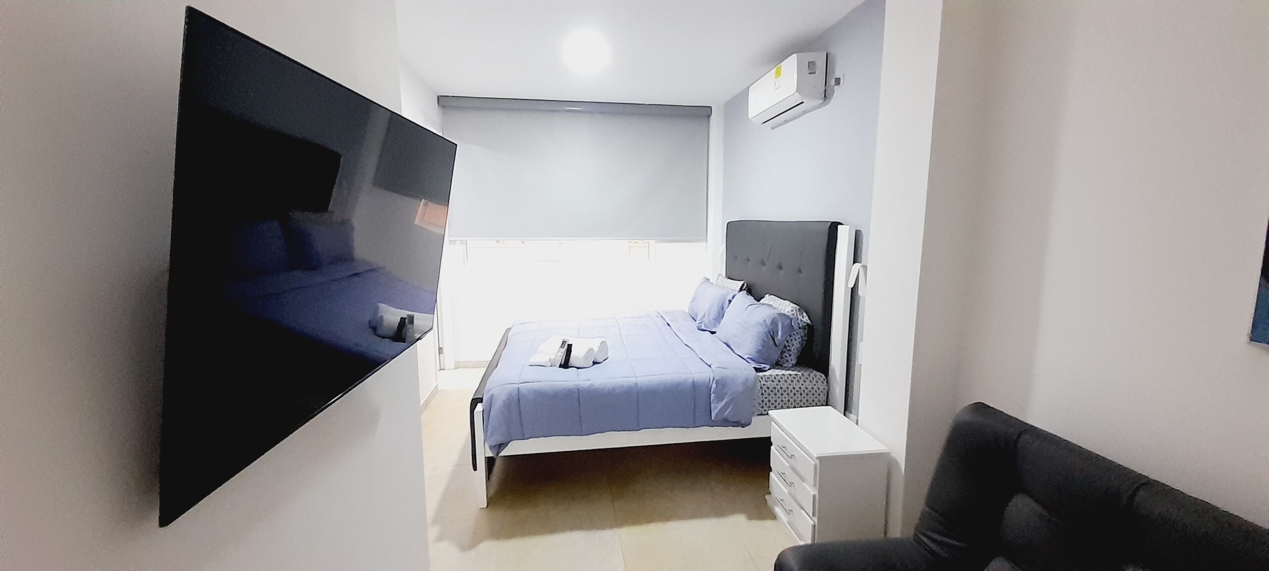A bedroom with a bed, bedside table, and a wall-mounted TV.