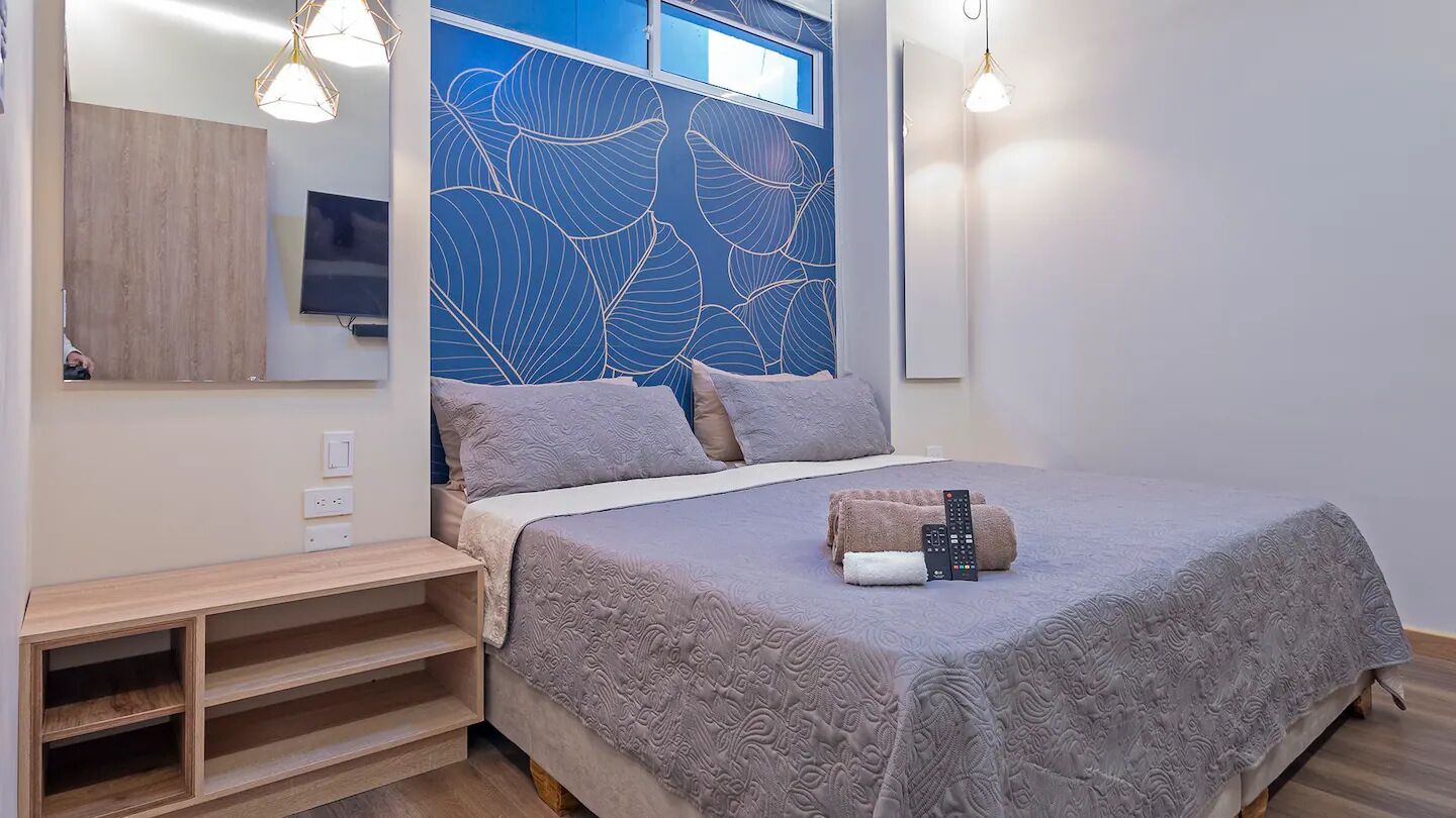 Ein Schlafzimmer mit einem Bett, einem Nachttisch aus Holz, einem Spiegel und einer Wand mit Blattmuster.