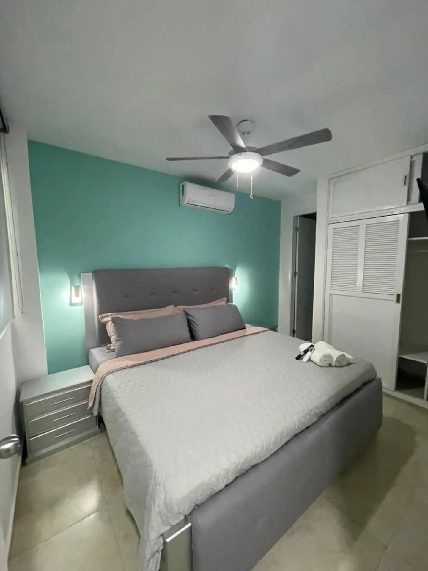 Une chambre à coucher comprenant un lit, un ventilateur de plafond, un climatiseur et une armoire.