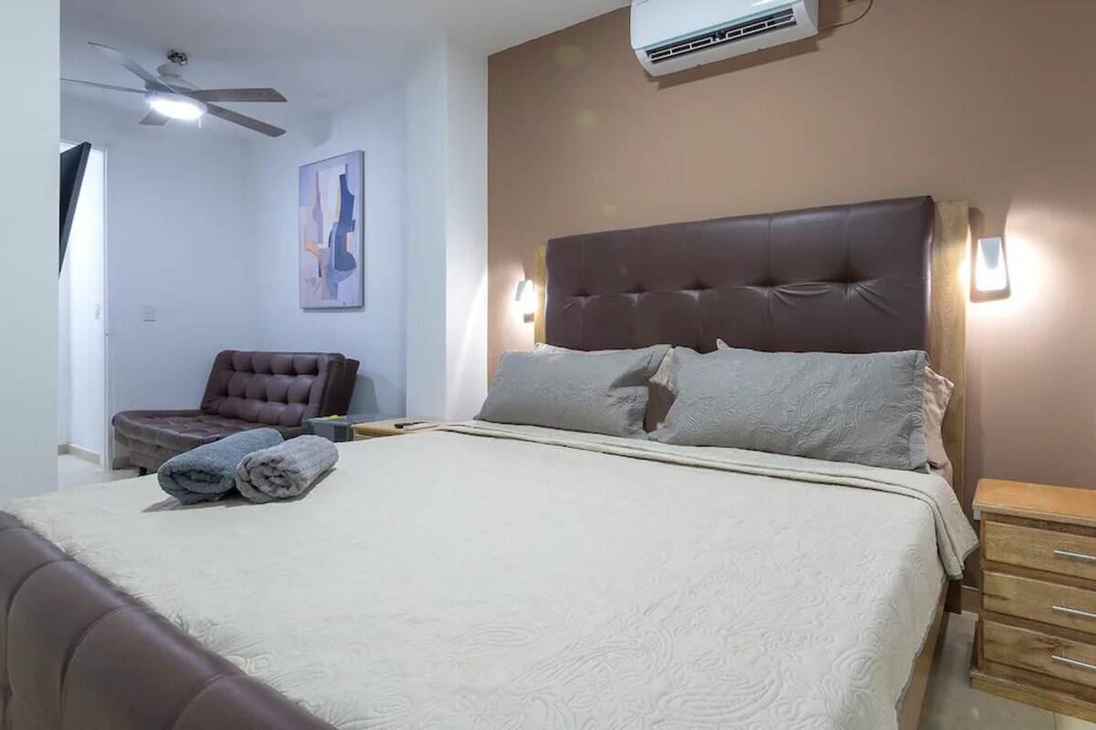 Ein Schlafzimmer mit einem großen Bett, einem Sessel, einem Nachttisch und einem Deckenventilator.