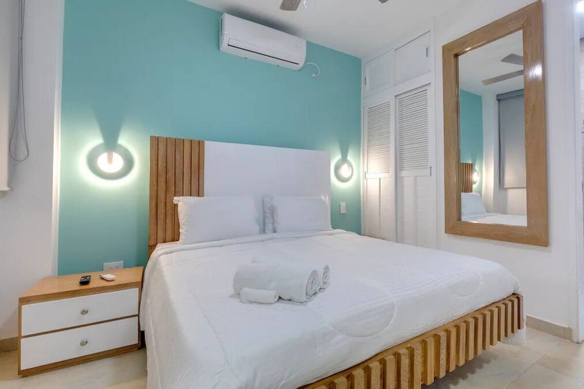 Ein Schlafzimmer mit Bett, Nachttischen, einem Spiegel und einem Badezimmer mit Waschbecken und Spiegel.