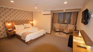 Une chambre d’hôtel avec un grand lit, un bureau avec une chaise, une télévision et une fenêtre avec des rideaux.