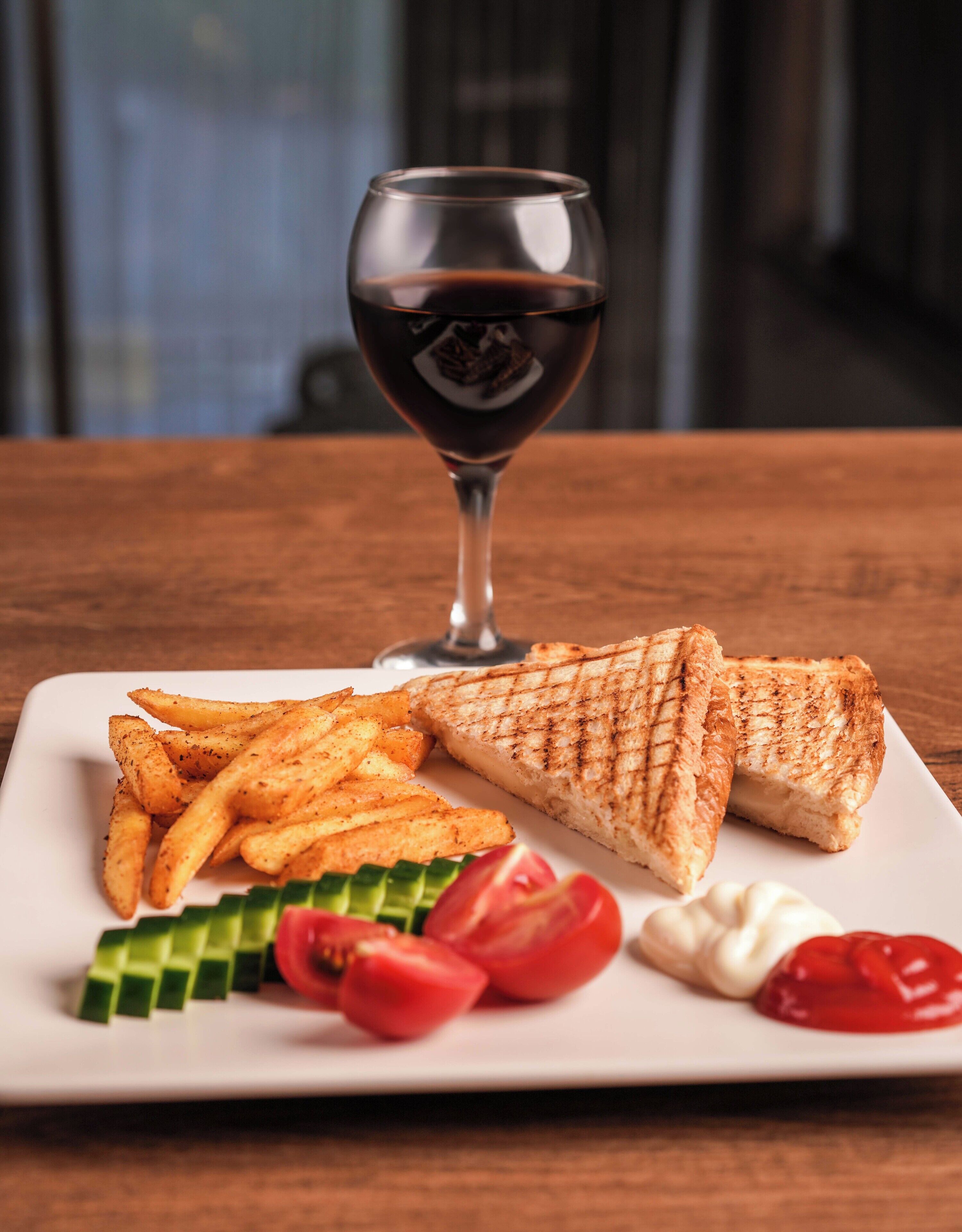 Um prato com sanduíche de queijo grelhado, batatas fritas e legumes sobre uma mesa de madeira.