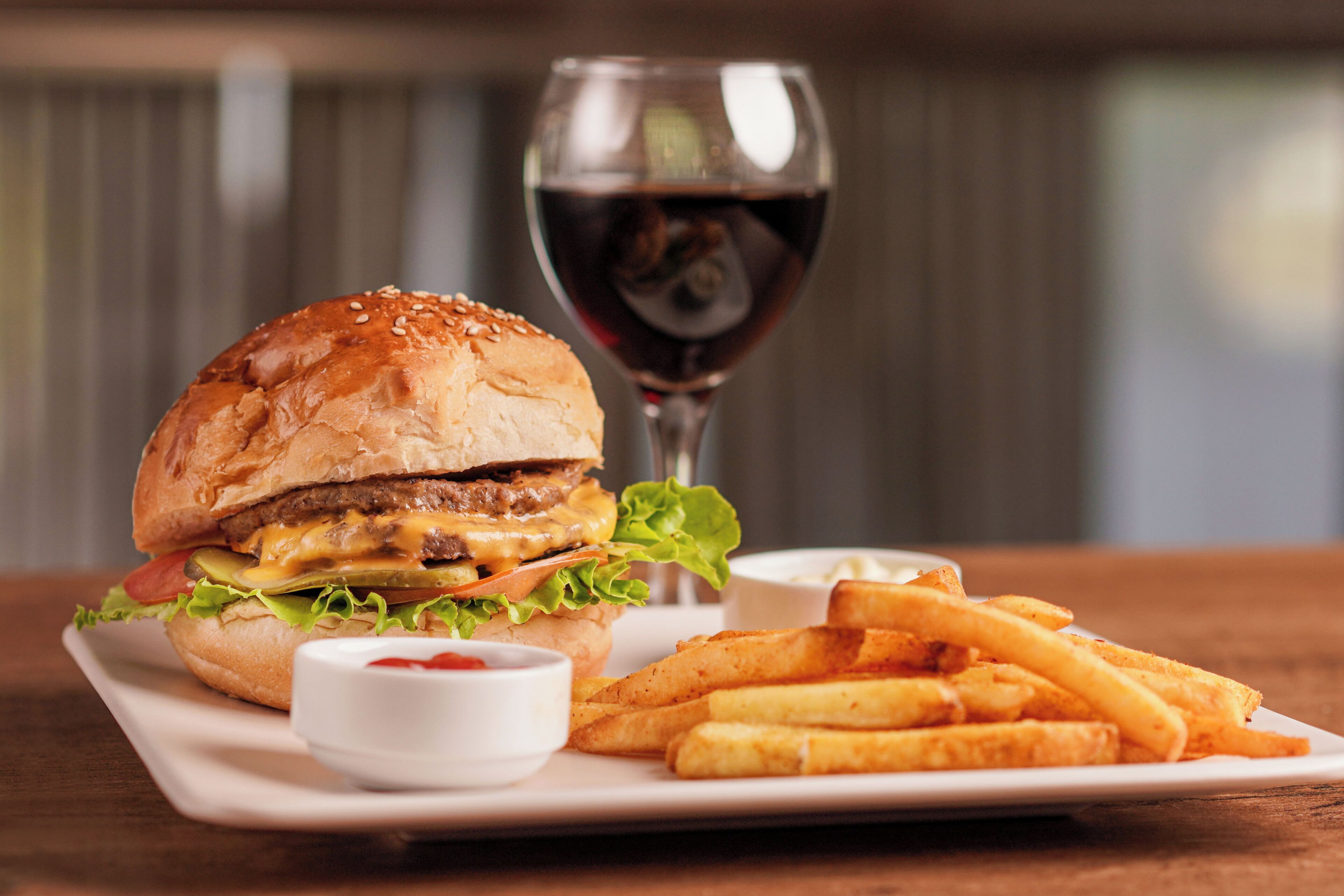 A burger with fries and a glass of red wine on a white plate.