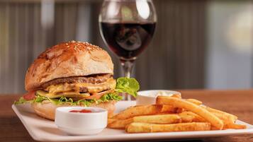 Una hamburguesa acompañada de papas fritas y una copa de vino tinto sobre un plato blanco.