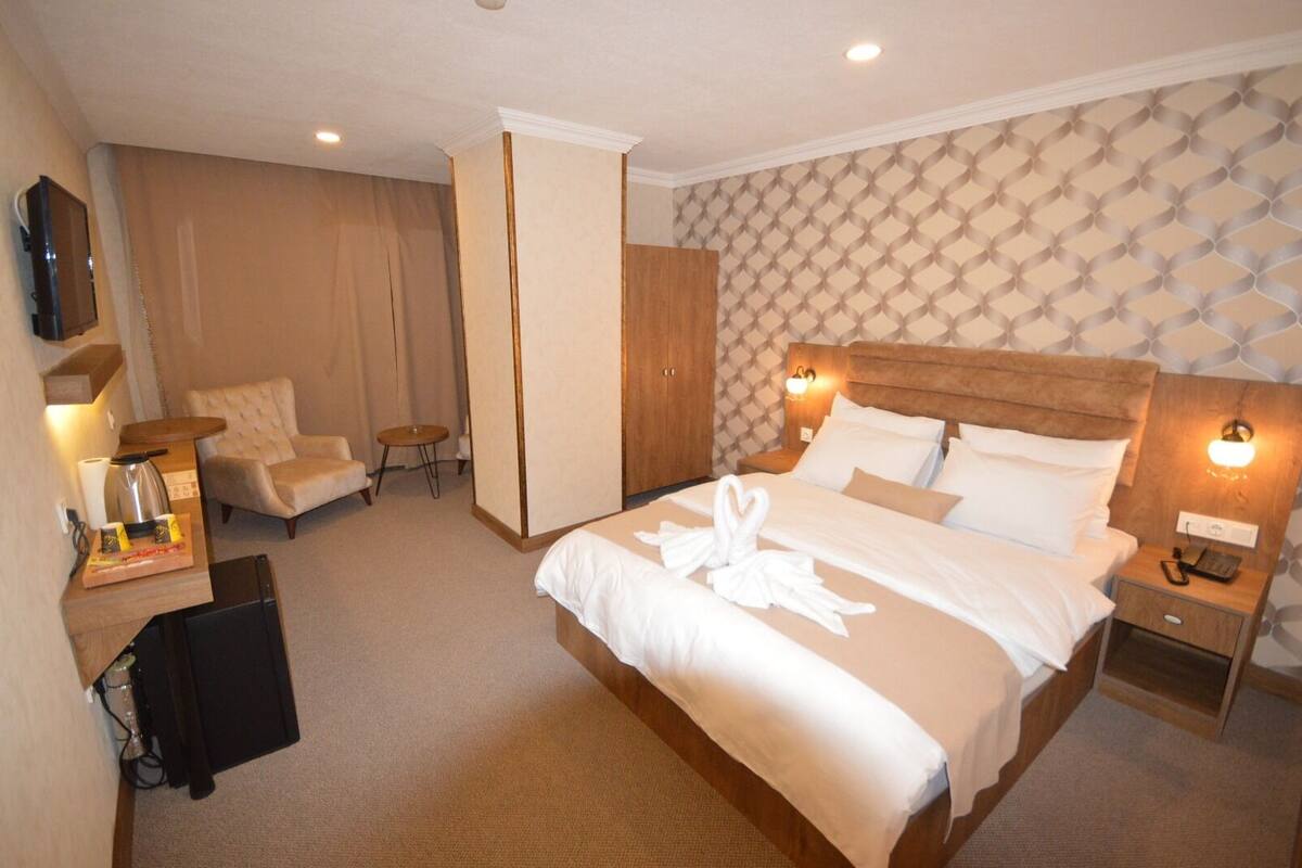 A hotel room with a large bed, a desk with a coffee maker, a chair, a wardrobe, and a TV on the wall.