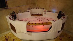 Un bain à remous parsemé de pétales de rose, un banc en bois et deux verres à vin.