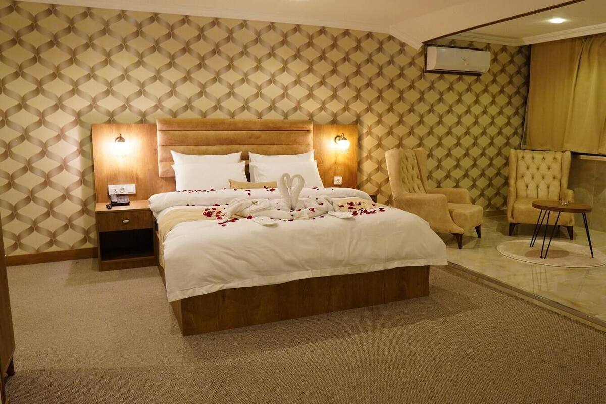 A hotel room with a large bed, two bedside tables, a seating area with chairs, and a glass partition.