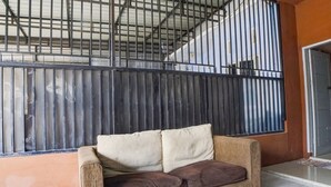 A room with a sofa against a wall with a metal fence, a tiled floor, and a door to the right. - Hotel O Penginapan Syariah Faster Inn (Medan)