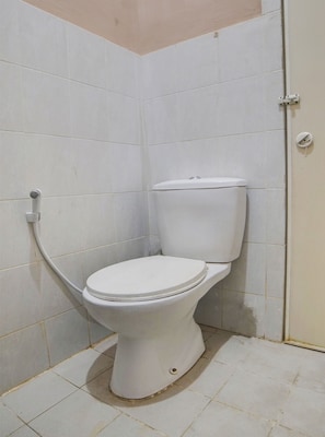 A white toilet in a corner of a room with white tiled walls and floor. - Hotel O Penginapan Syariah Faster Inn (Medan)