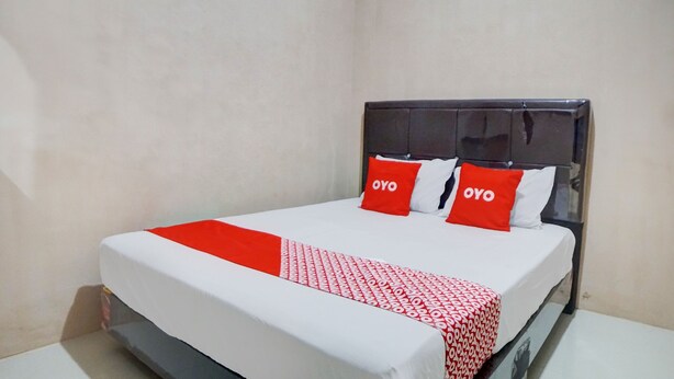 A hotel room with a bed, white and red bedding, and two red pillows with the word "OYO" on them. - Hotel O Penginapan Syariah Faster Inn (Medan)