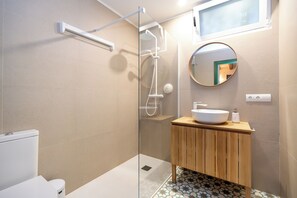 Un baño moderno con ducha de vidrio, tocador de madera y espejo redondo.
