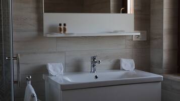 A modern bathroom with a white sink, two towels, a mirror above the sink, and a shelf with toiletries.