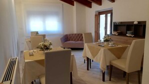 Uma área de refeições com uma mesa posta para quatro pessoas, um sofá e uma cozinha com uma prateleira.