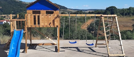 Una estructura de juegos de madera con un tobogán azul, columpios y una red de escalada.