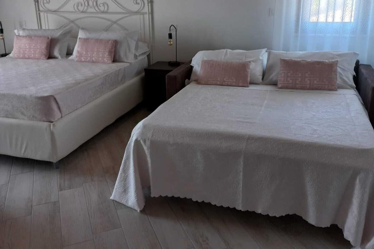 Two beds with white linens and pink pillows in a room with wooden flooring and a sloped ceiling.