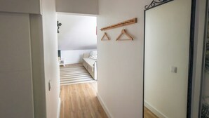 A hallway with a wooden floor, a white wall, and a door on the right. There is a hanging rack with wooden hangers on the wall. - SandybeachApartment2 in the Golden Island  (Vila Baleira)