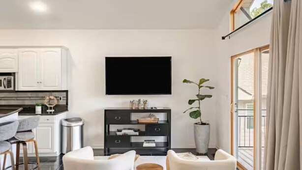 A modern living room with a flat-screen TV, a dining area with bar stools, and a kitchen with white cabinets. - Spacious Lake Hamilton House with Pool and Hot Tub! (Hot Springs)