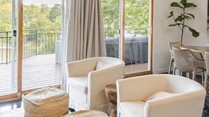 A modern living room with white armchairs, a large window with a view of a balcony, and a dining area with wicker chairs. - Spacious Lake Hamilton House with Pool and Hot Tub! (Hot Springs)