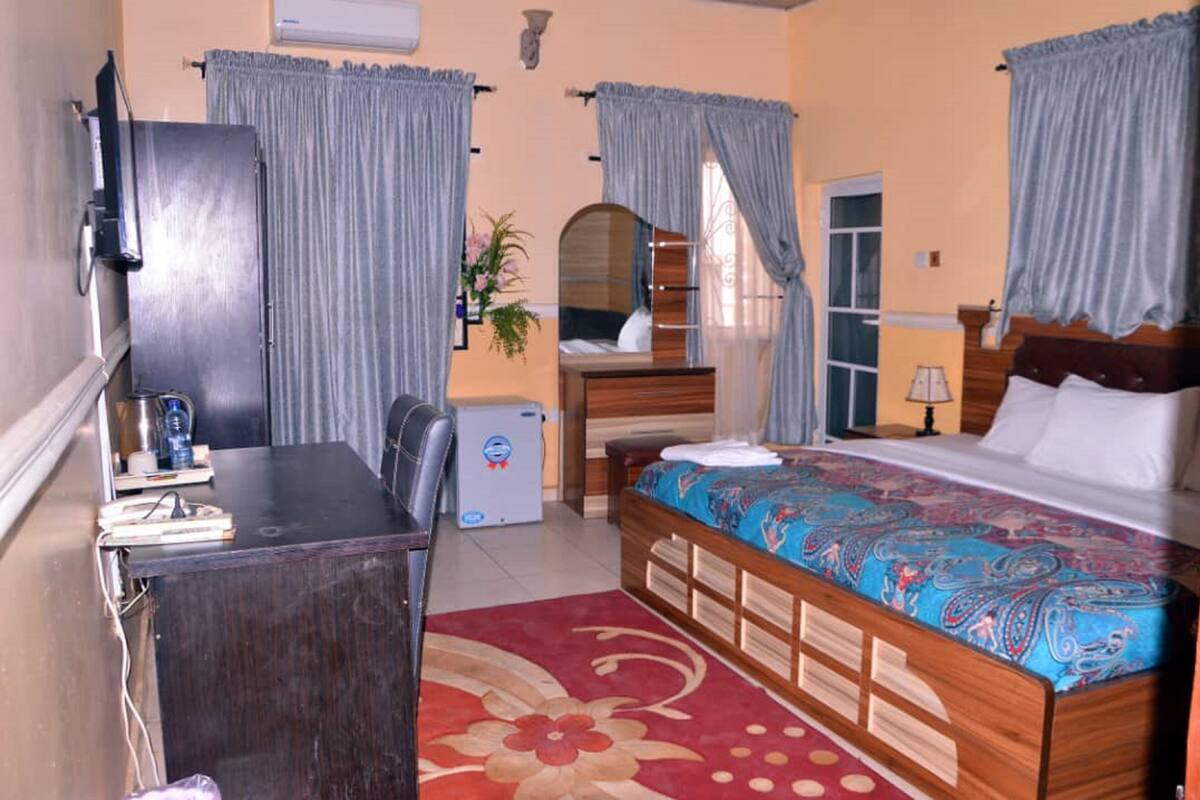 A bedroom with a bed, a desk, a chair, a dresser, and a mirror.