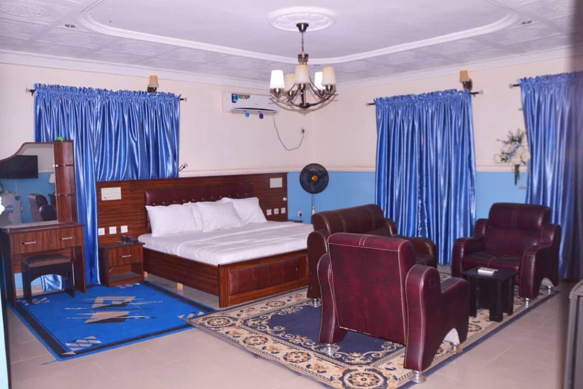 A hotel room with a wooden bed, a desk with a chair, a sofa, and a fan.