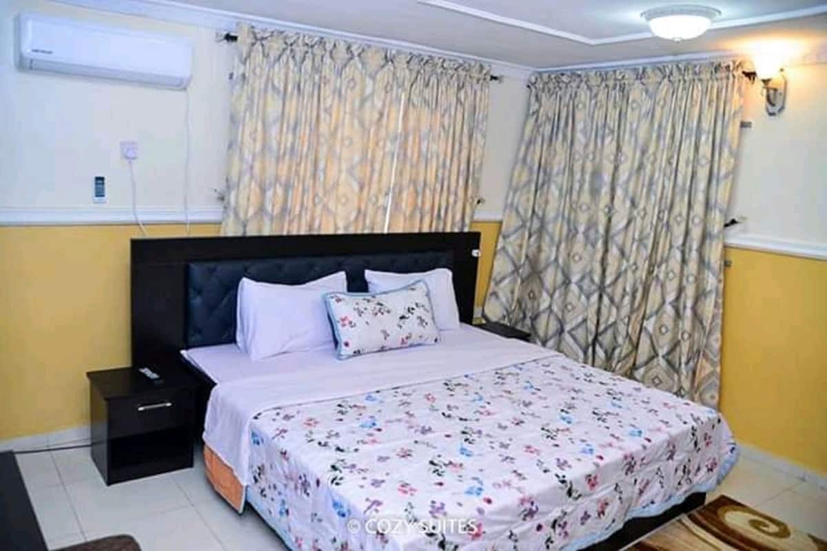 A bedroom with a bed, a nightstand, a wall-mounted air conditioner, and patterned curtains.