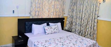 A bedroom with a bed, a nightstand, a wall-mounted air conditioner, and patterned curtains.