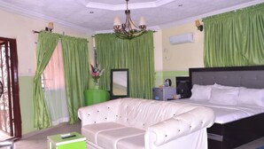 A hotel room with a large bed, a white sofa, a small green table, and a chandelier. - Cozy Suites (Akure)