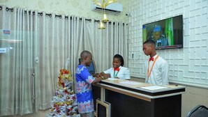 A reception area with a reception desk, a television mounted on the wall, and a Christmas tree. - Cozy Suites (Akure)