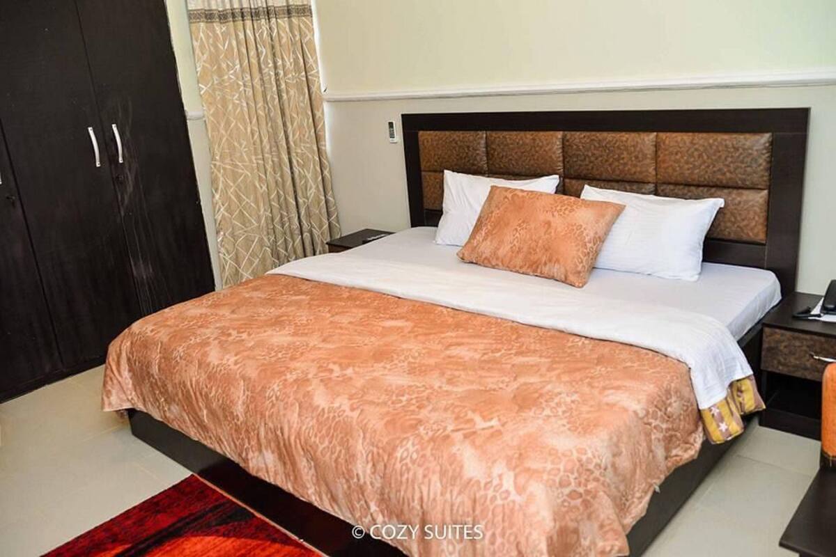 A neatly made bed with a patterned bedspread, a headboard with a textured design, and a dark wardrobe.