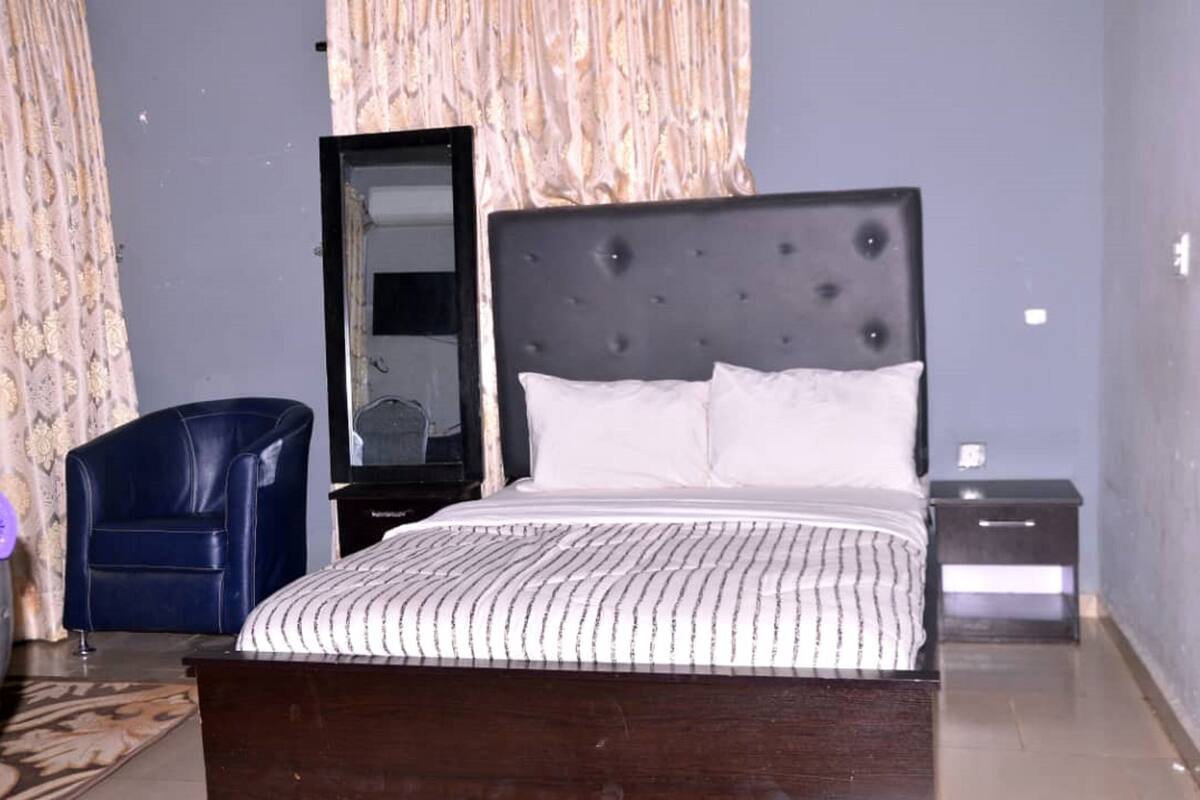 A bedroom with a large bed, a chair, a nightstand, and a mirror.