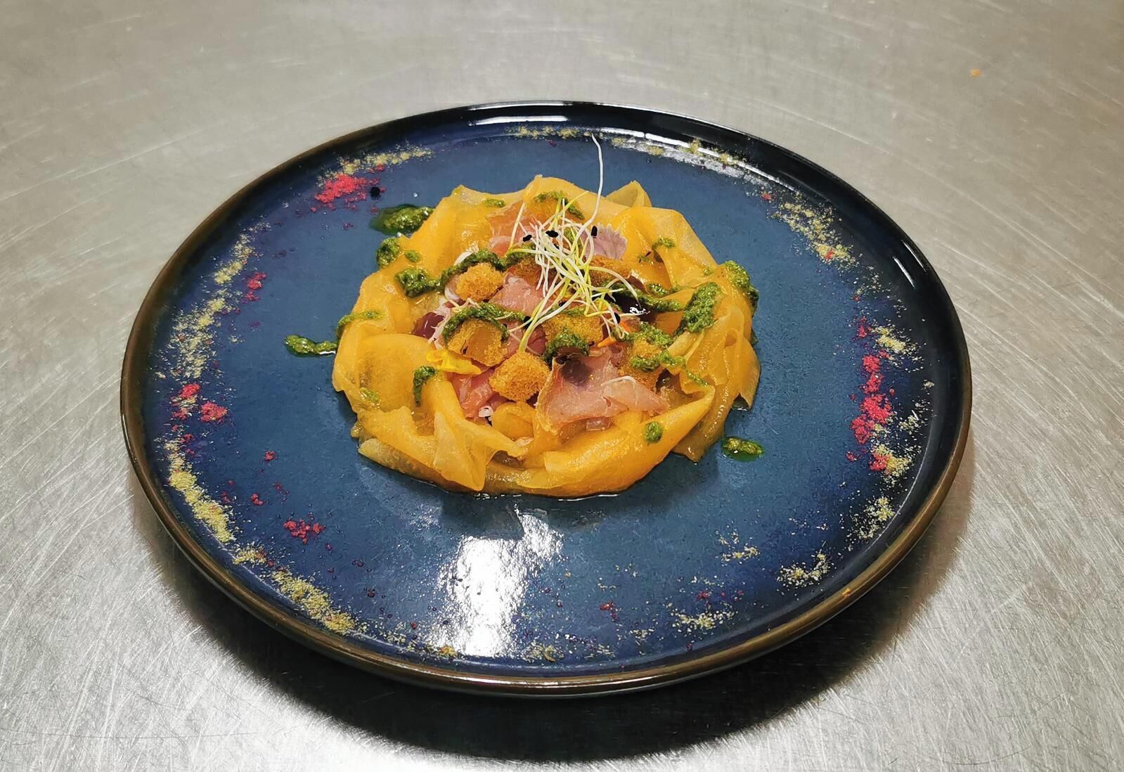 A plate of food with a blue rim and a central yellow dish, garnished with green herbs and sprouts.