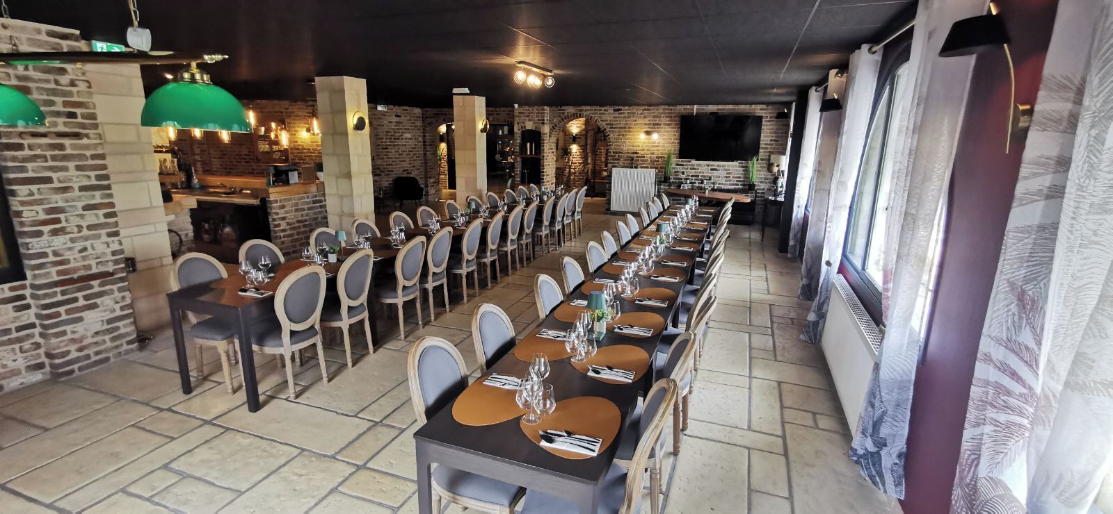 A long dining table with chairs, a brick wall, and hanging lights.