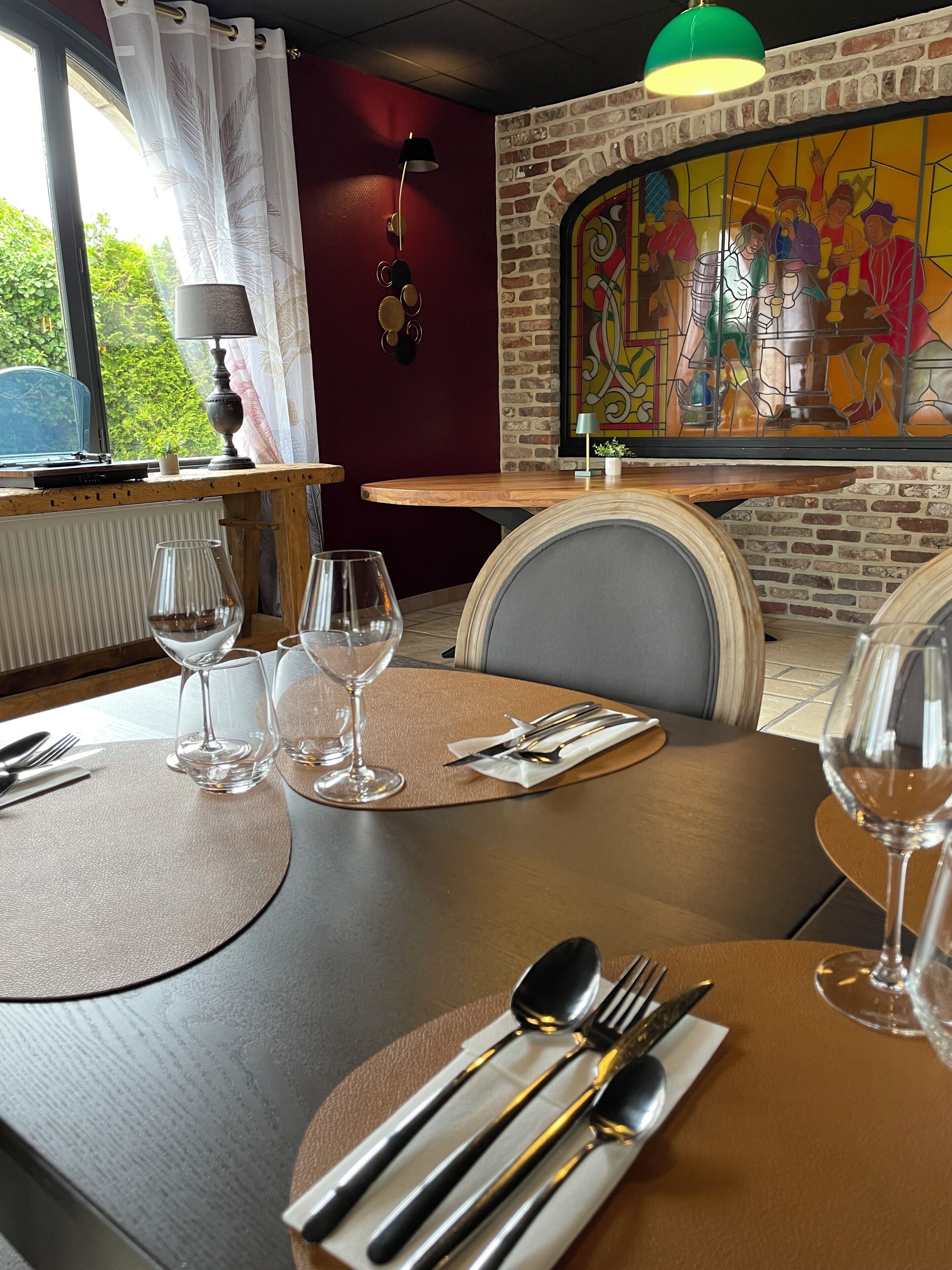 Comedor con una mesa dispuesta para dos, que incluye un ventanal con vidrieras, un radiador y vistas a la vegetación exterior.