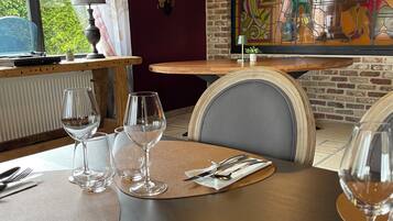 Comedor con una mesa dispuesta para dos, que incluye un ventanal con vidrieras, un radiador y vistas a la vegetación exterior.