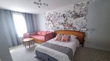 A hotel room with a bed, a sofa, a chair, and a floral wallpaper.