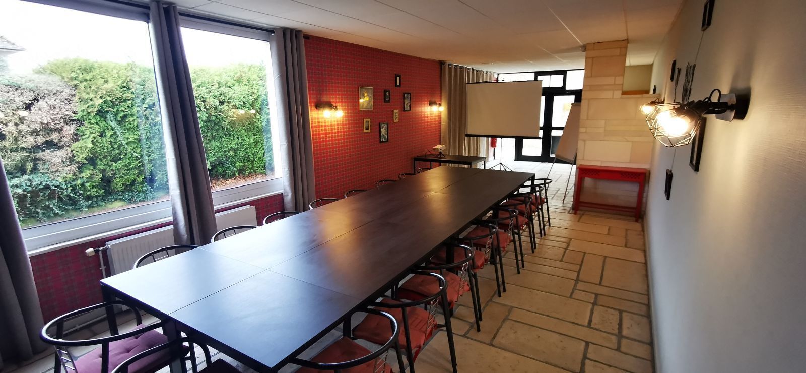 A conference room with a long table, chairs, a projector screen, and a view of greenery outside.