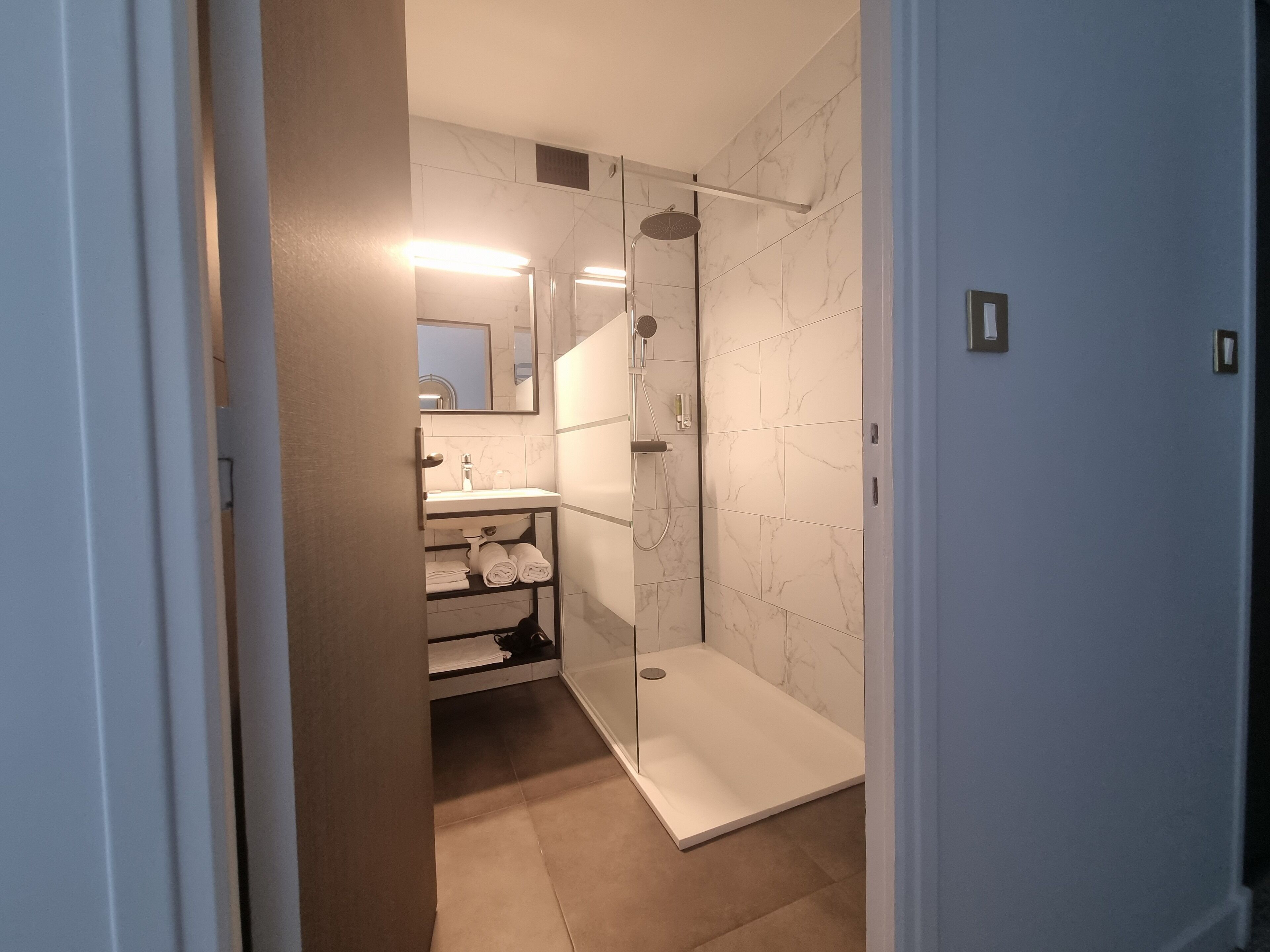 Een moderne badkamer met een douchecabine, een wastafel met spiegel en keurig opgevouwen handdoeken op een plank.