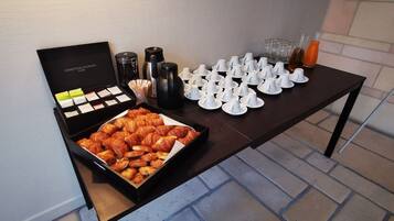 A table with a box of chocolates, a tray of croissants, and several coffee cups and glasses.