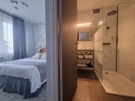 Una habitación de hotel con cama, baño con ducha y espejo.