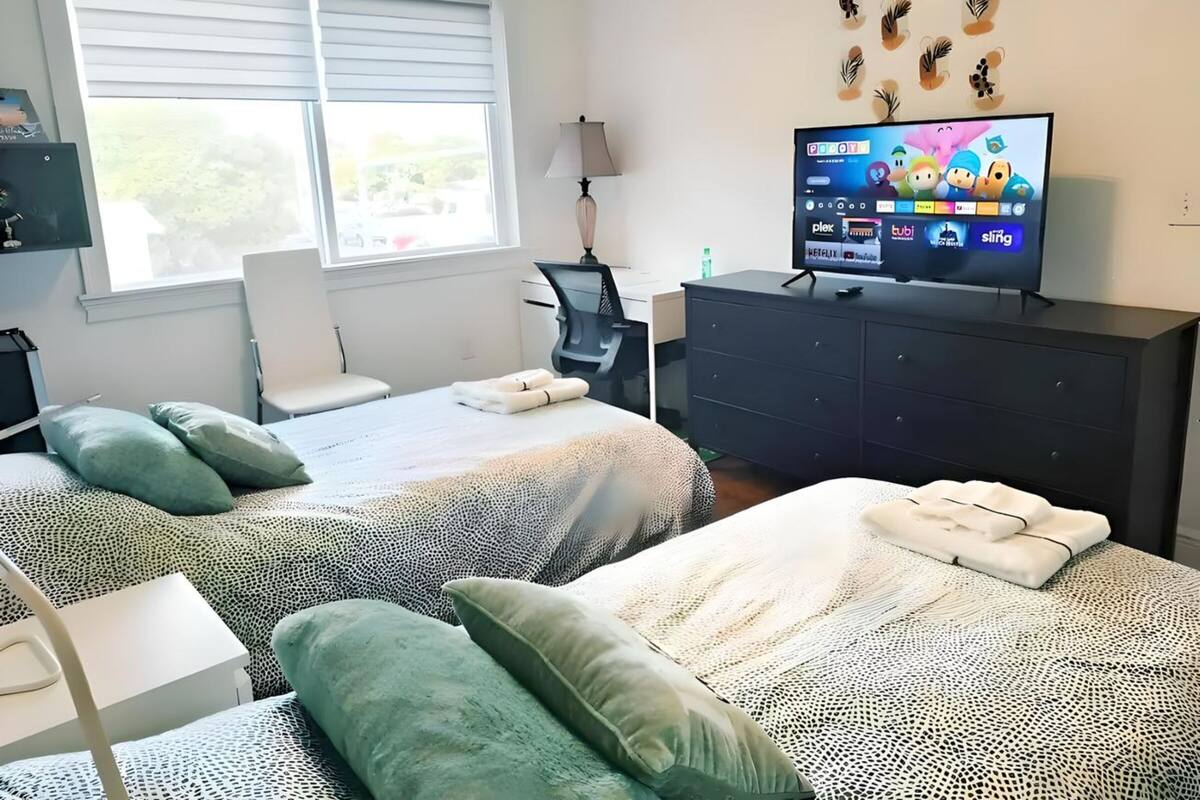 A hotel room with two beds, a desk, a chair, a TV, and a window with blinds.